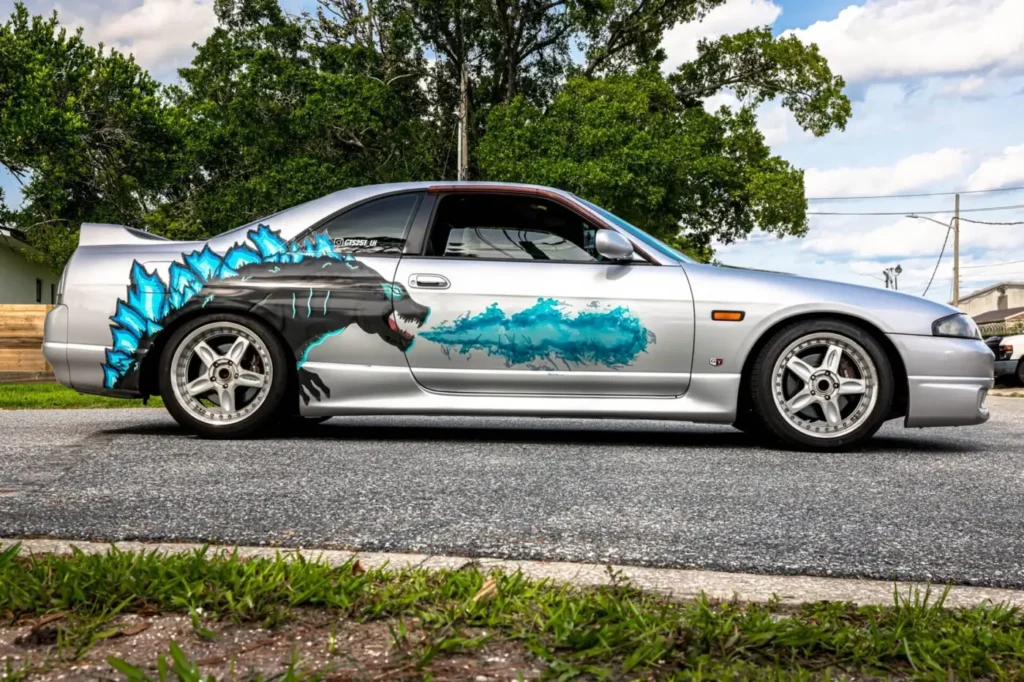 Silver Nissan Skyline with a custom Godzilla graphic wrap, side view