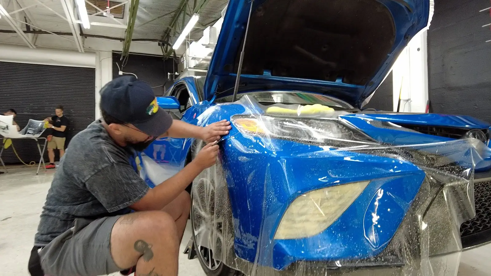 Installer applying STEK paint protection film to a blue car bumper
